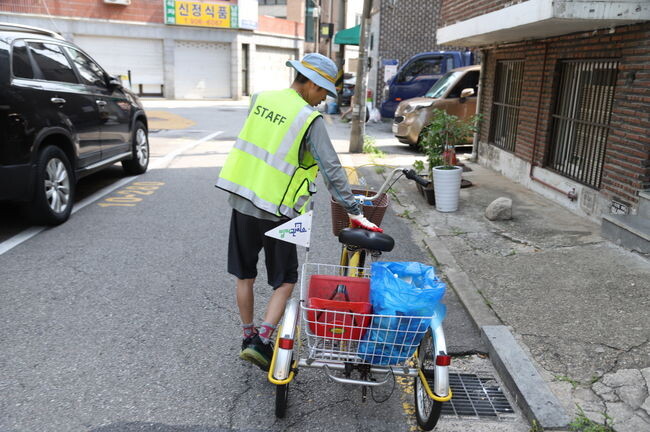강북구 빌라관리사무소 담당매니저가 전용 자전거와 청소도구를 사용해 빌라 주변과 골목 일대를 청소하고 있다.