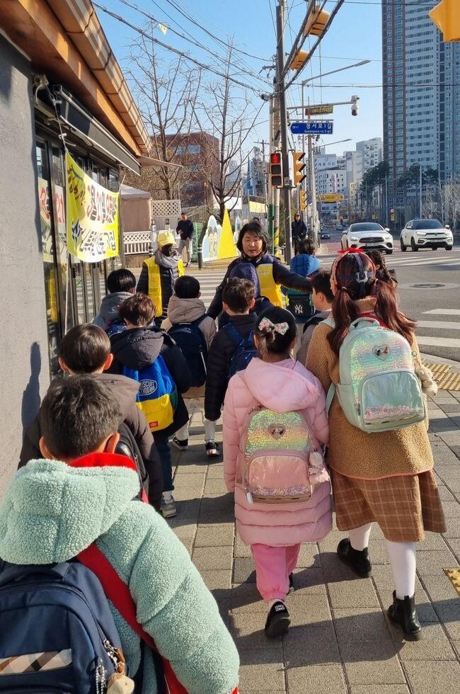 어린이들이 교통안전지도사와 함께 등교하고 있다.